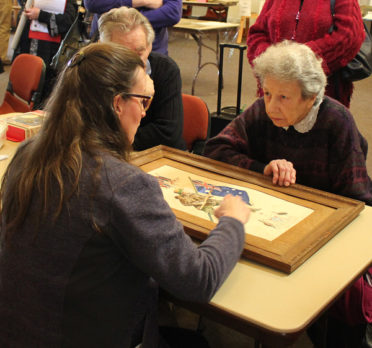 People around a table looking at a framed work.