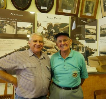 Image: two men in room in front of signs and photos