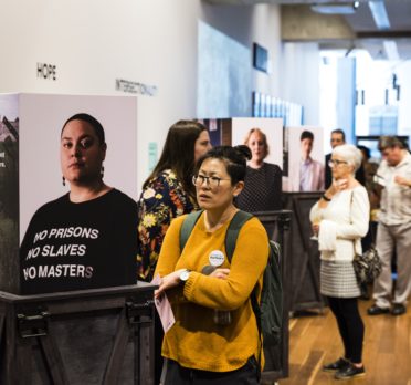 People looking at display of images on plinths in a gallery space.