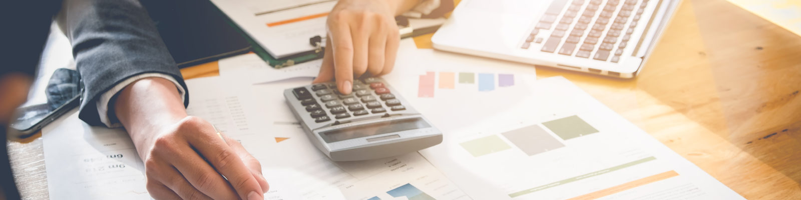 Person sitting at desk with a calculator looking at graphs.