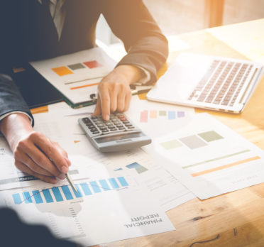 Person sitting at desk with a calculator looking at graphs.