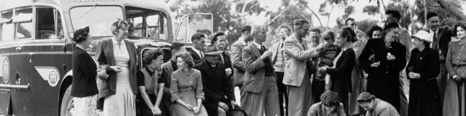 Group of people standing in front of a bus surrounded by gum trees.