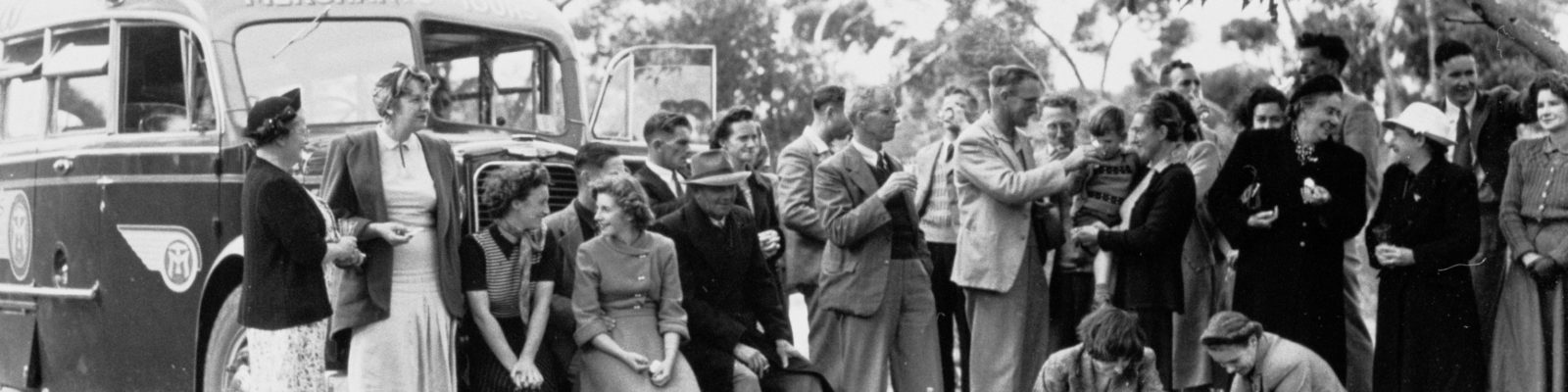 Group of people standing in front of a bus surrounded by gum trees.