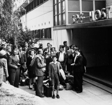 Group of people with suitcases in front of a building.