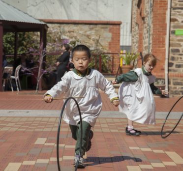 Young children running outside with hoops.