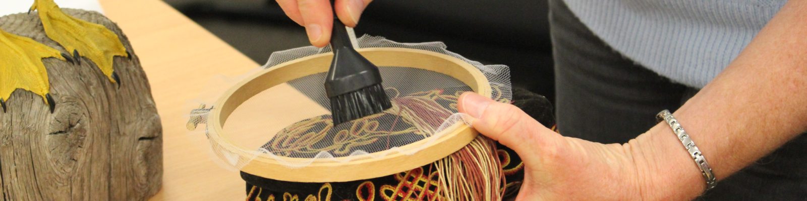 Pair of hands holding a small vacuum attachment on top of a gauze film over an embroidered cap.