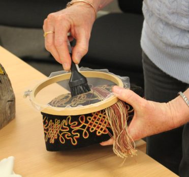 Pair of hands holding a small vacuum attachment on top of a gauze film over an embroidered cap.