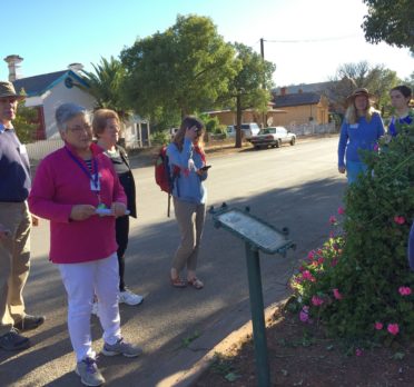 Group of people standing around an interpretive sign on the side of a street. .