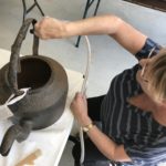 A woman with a vacuum cleaner brush attachment cleaning an old kettle.