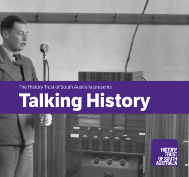 Man standing at microphone with purple banner accross.