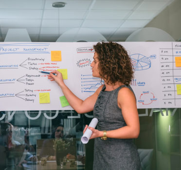 Woman standing at flow chart on large paper with sticky notes.