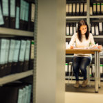 Young woman sitting at a desk surrounded by shelves of folders.
