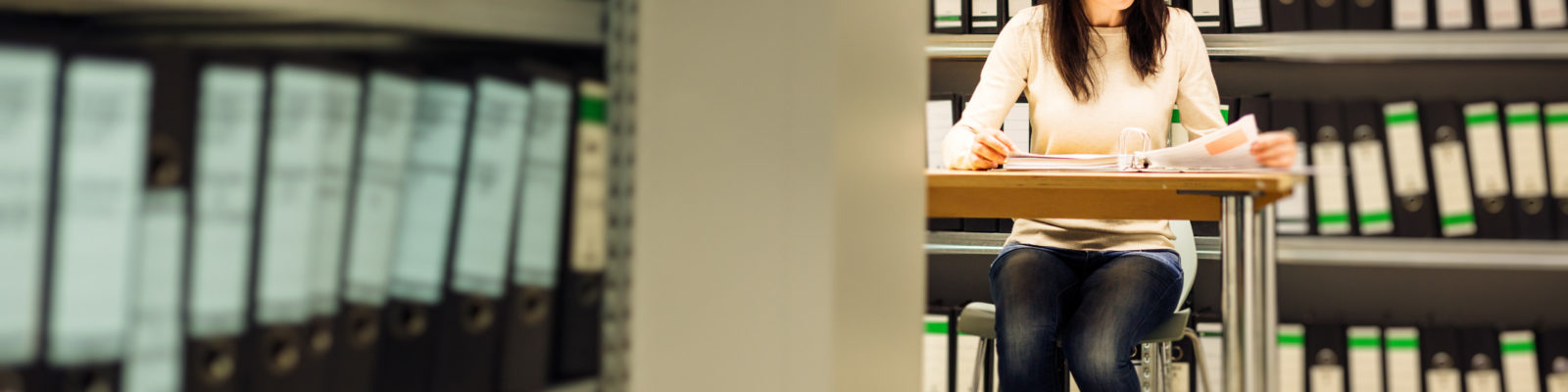 Young woman sitting at a desk surrounded by shelves of folders.