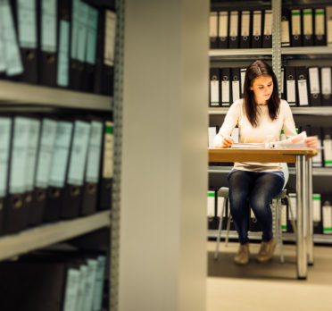 Young woman sitting at a desk surrounded by shelves of folders.