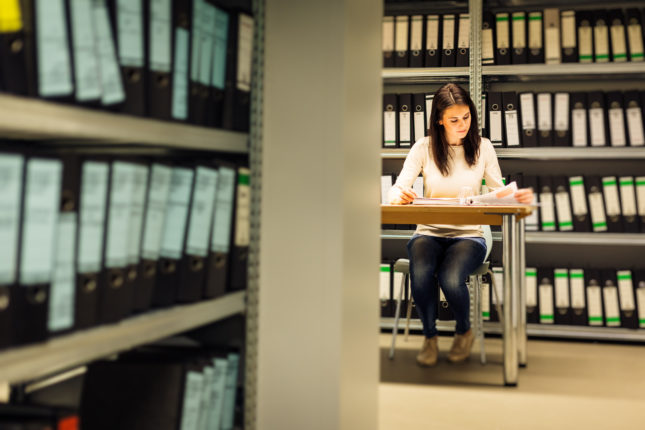 Young woman sitting at a desk surrounded by shelves of folders.