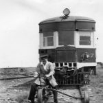 Man on a railway trike on tracks in front of a train.