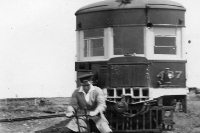 Man on a railway trike on tracks in front of a train.