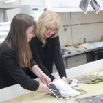 Two women holding large photograph in a table of water