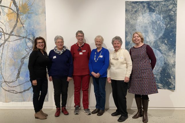 Group of smiling women in front of artworks in a gallery