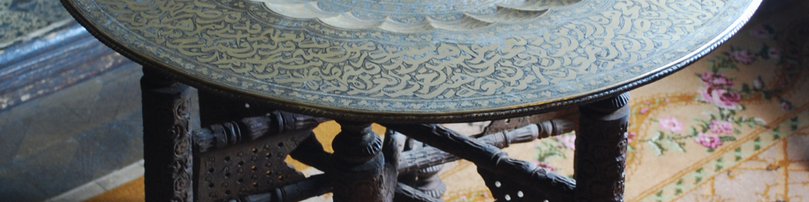 View looking down onto decorative metal tray round table top on carved wooden legs