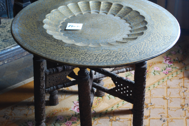 View looking down onto decorative metal tray round table top on carved wooden legs