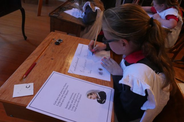 Child at old fashioned school desk writing with pen and ink