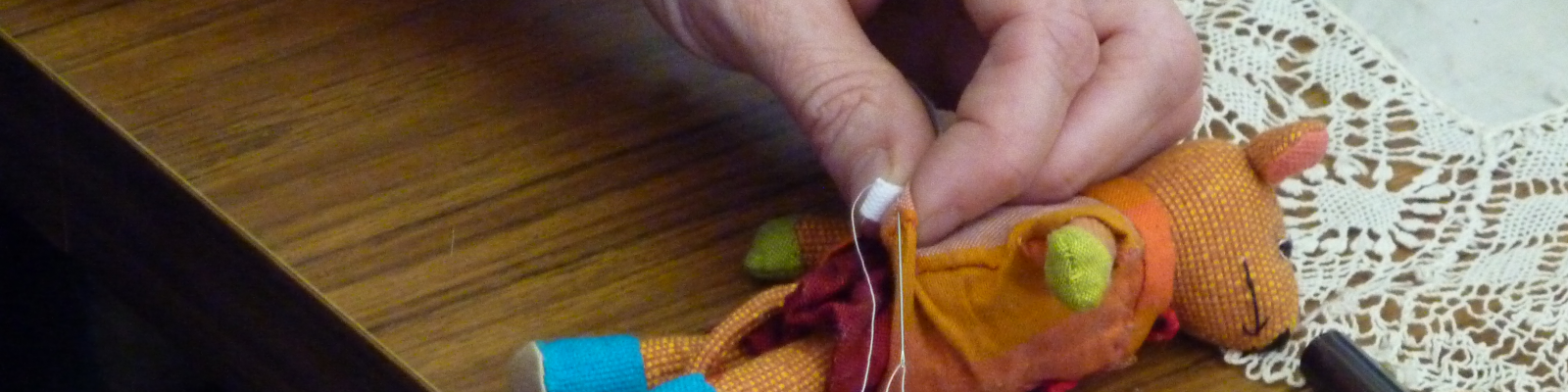 close up of hand holding needle and thread with a small soft toy