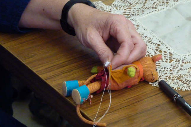 close up of hand holding needle and thread with a small soft toy