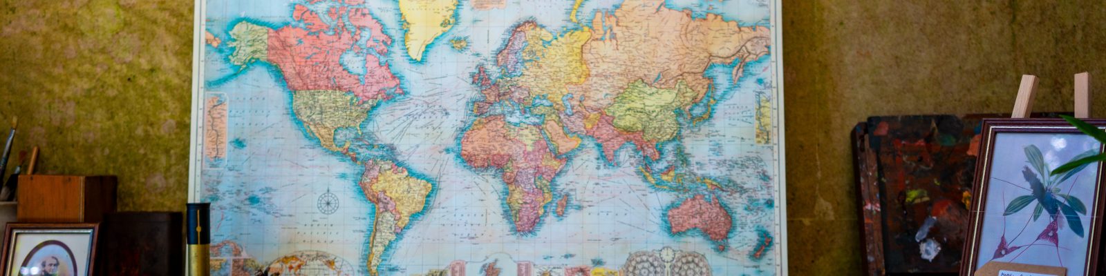 Map of the world sitting at the back of a cluttered desk covered in books and art materials.
