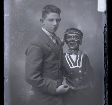 Black and white portrait of a young boy with a ventriloquist doll, circa 1920s.